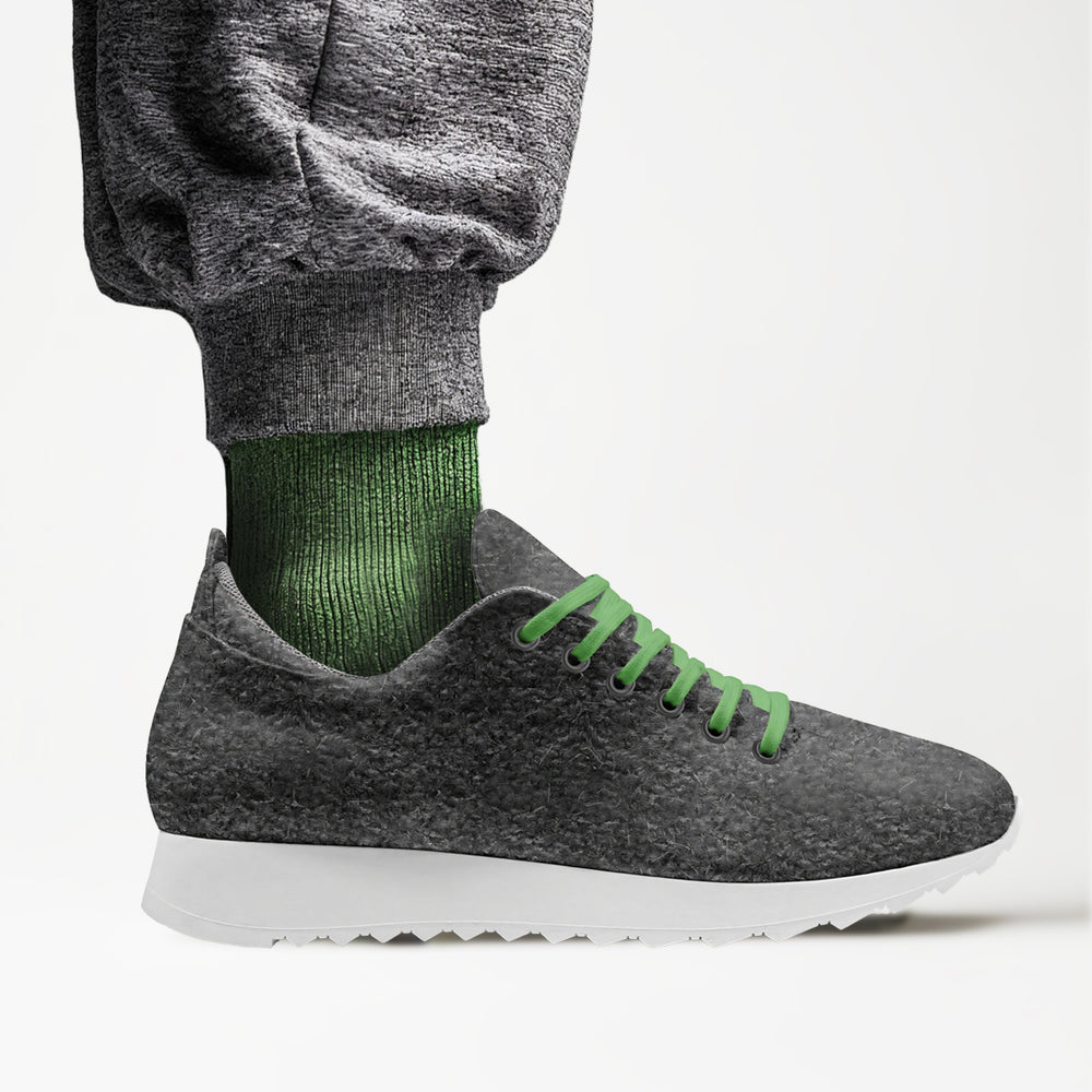 Eco-friendly, vegan 'Align' sneakers with a gray textured upper and green laces, paired with sweatpants, showcasing sustainable luxury.