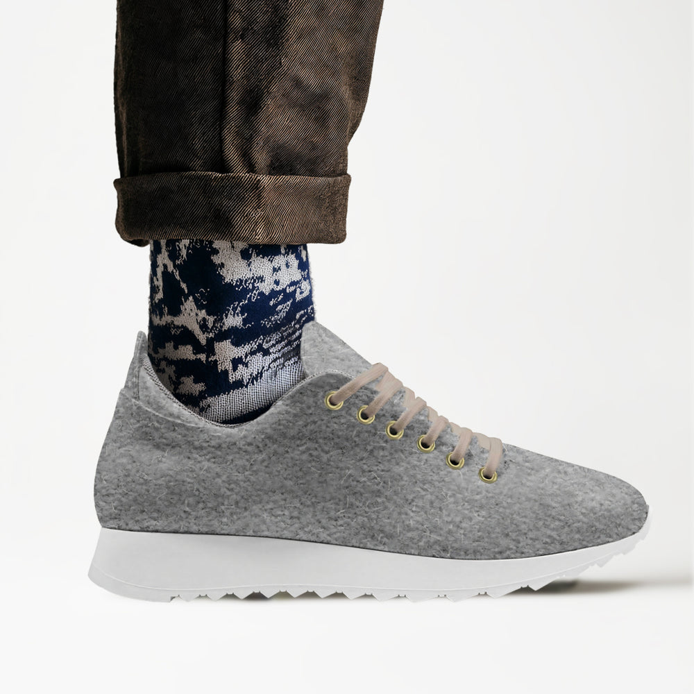Soft grey wool low-top sneakers with white soles and comfortable texture, matched with rolled-up brown trousers.