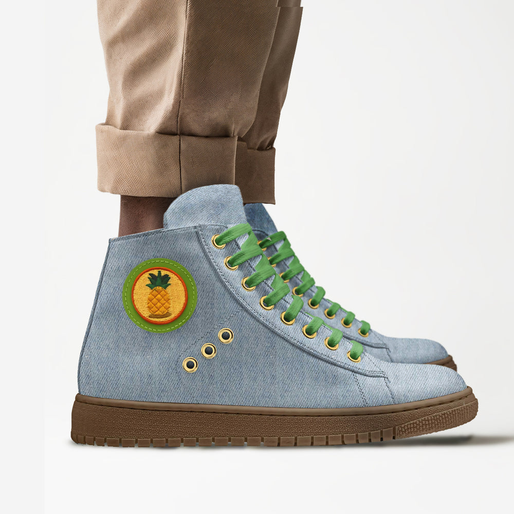 Sustainable 'Wave' high-top sneakers in denim fabric with a vibrant pineapple patch, featuring green laces and gold eyelets for eco-conscious style, paired with rolled khaki pants. 